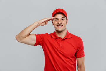 Young delivery man wearing uniform saluting and smiling at camera