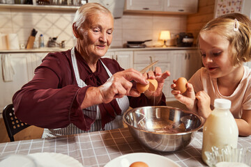 Elderly female teaching child how to break an egg