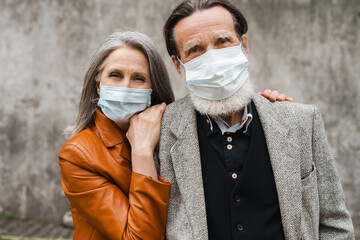 White senior couple in face masks hugging and looking at camera