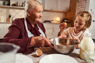 Girl breaking an egg into a steel bowl with granny
