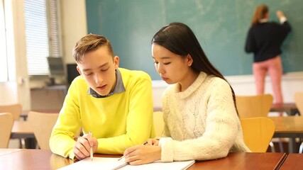 Smiling Chinese girl student helping her friend prepare for exam in college classroom