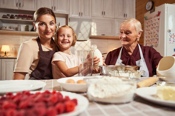 Joyful girl lifting milk bottle beside her mother and granny