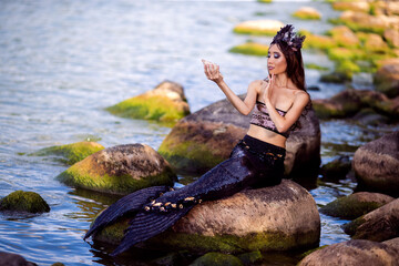 Asian Mermaid Posing With Shell Near Ocean Shore on Rocks While Wearing Seashell Decorated Crown...