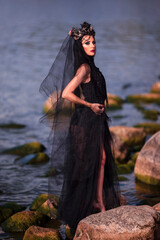 Dance Concepts. Sensual Caucasian Brunette Female Dancer in Black Light Dress Wearing Artistic Seashell Crown And Dancing Against Sea