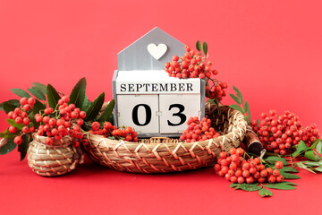 Calendar for September 3 : the name of the month in English, cubes with the numbers 0 and 3 on a decorative tray, branches of red mountain ash around on a crimson background, side view