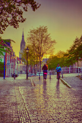 Obraz premium Dutch Travel Ideas. Friendly Couple in Holland Traveling on Bicycles in Old City Delft During Pouring Rain with Grey Clouds.