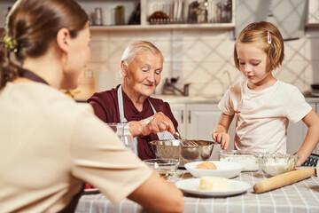 Obraz na płótnie Canvas Kid helping her elderly grandmother in making dough