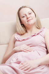 Naklejka premium Young Romantic Caucasian Pregnant Blond Female Resting on Couch With Hands on Belly Posing Indoors.