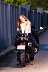 Fototapeta na wymiar Sensual Caucasian Female Motorcyclist Biker Leaning On Sport Bike Outdoor While Sitting Back To Front Outdoors.