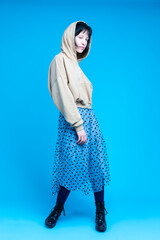 Naklejka premium Young Dancing Brunette Girl in Street Clothing Posing In Headphones and Hoodie in Dance Pose Over Blue Background.