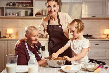 Excited mother looking at camera while her daughter mixing dough