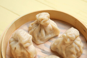 Bamboo steamer with tasty dumplings on color wooden background, closeup