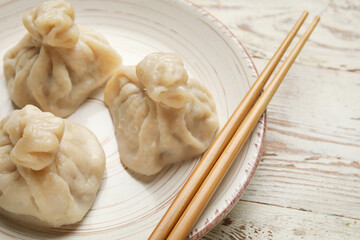 Plate with tasty dumplings and chopsticks on light wooden background, closeup