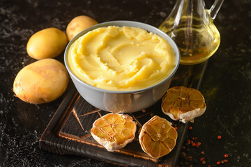 Bowl of tasty mashed potatoes with garlic and vegetables on dark background