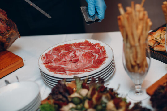the waiter cuts the hamon with a knife and holds a piece of ham in the clamp in his hand.