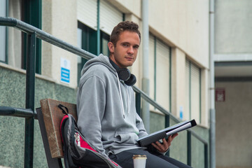 young student with headphones sitting in front of institute or university