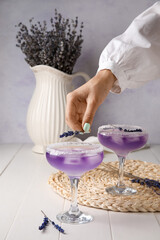 Woman decorating glass of fresh cocktail with lavender on table, closeup
