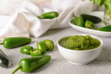 Bowl of Tomatillo Salsa Verde sauce and jalapeno pepper on light background