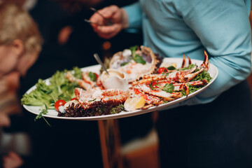 a waiter in a restaurant holds seafood dishes and serves a table catering Concept Healthy food...