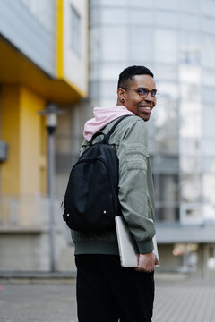 Image of young man with backpack walking in the city holding laptop computer.
