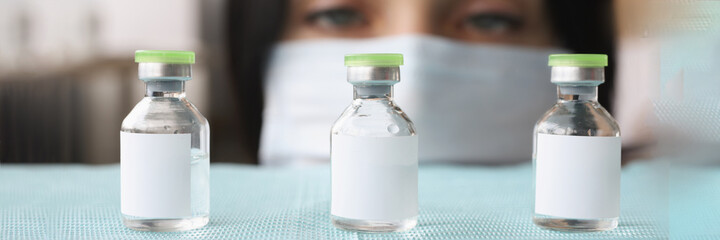 Woman pharmacist in protective medical mask selecting glass bottles with liquid closeup