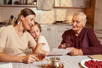 Child embracing mother arm, who praising her picture with granny