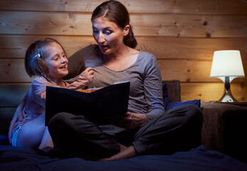 Fototapeta premium Girl enjoying bedtime stories from her mum