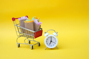Shopping cart with paper bags and vintage clock on a yellow background.