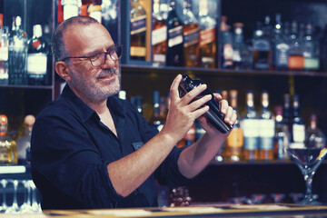 Elderly bartender male with glasses makes a cocktail