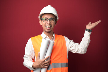 Young Asian architect wearing helmet and holding project paper plan pointing with hand to the sid