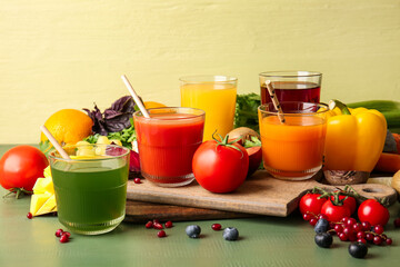 Glasses with healthy juice, fruits and vegetables on color wooden background