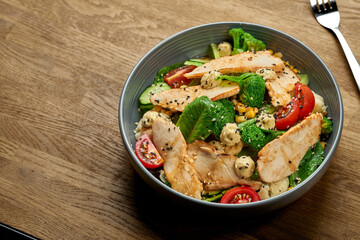Diet salad with chicken, broccoli and cherry tomatoes in a bowl on a wooden background. Close up, selective focus with noise grain