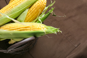Basket with fresh corn cobs on fabric background, closeup