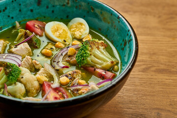 Green soup with broccoli and cauliflower, onion, chicken and egg in a bowl on a wooden background