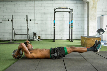 young african american man doing crunches with a ball in the gym - Powered by Adobe