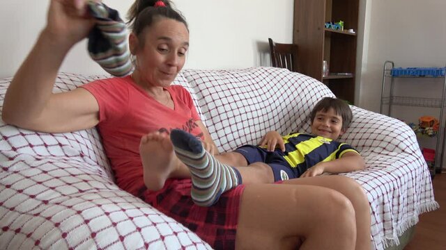 4K Playful mother takes off socks of boy resting on sofa and tickles him
