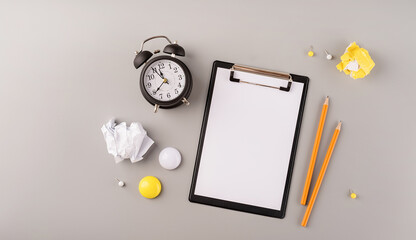 Blank paper on clipboard, white alarm clock and stationery top view on gray background