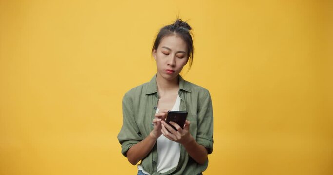 Attractive Asian youth isolated lady on empty space use smart phone feel boring emotional with doubtful and skeptical online news with serious face thinking text sending message on yellow background.
