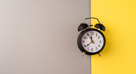 Black retro alarm clock isolated on double yellow and gray background with copy space
