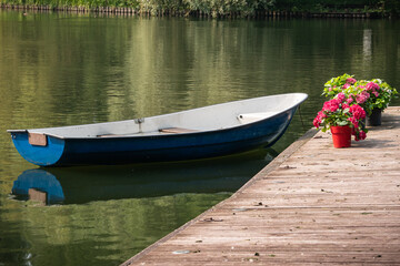 A boat at a wooden pier on the lake, on which there are house flowers in pots for transportation