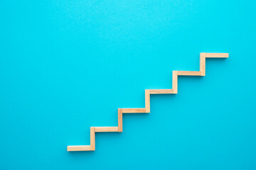 Flat lay of wooden blocks in shape of staircase step on blue background with copy space. Growth or...