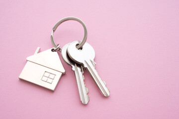 Silver house key with house keychain on pink background with copy space. Dream new house buying, real estate property business concept.