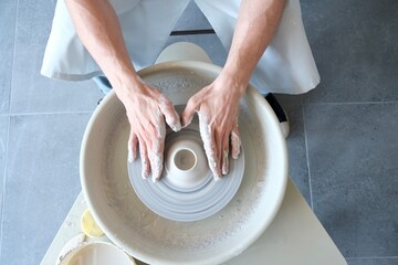 A young brutal man makes a product from white clay on a potter's wheel. The concept of creativity and privacy. A potter's wheel. 