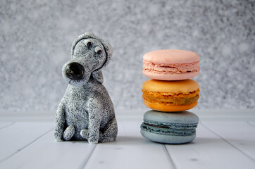 cute funny toy dog looks at delicious sweet macaroons lying nearby. Concept: diet, avoiding sweets, proper nutrition, making confectionery. Humorous postcard, poster, space for text - obrazy, fototapety, plakaty
