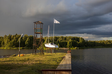 Boat on a pedestal. Cloudy sky over the river in the evening. Picturesque landscape with clouds and a river. Bright green grass in the foreground.