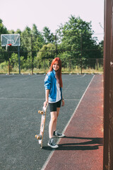 Portrait of a charming girl with a skateboard in her hand on a sports field