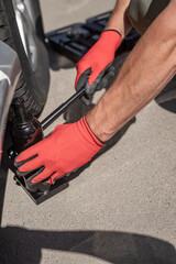 Obraz premium Hydraulick jack is put under car by male hands.