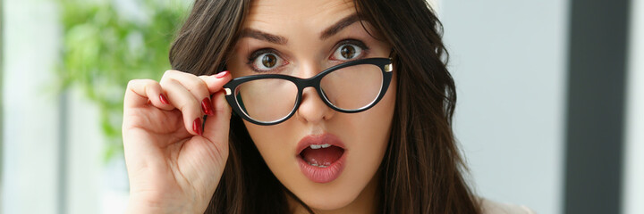 Young surprised woman adjusting glasses for vision