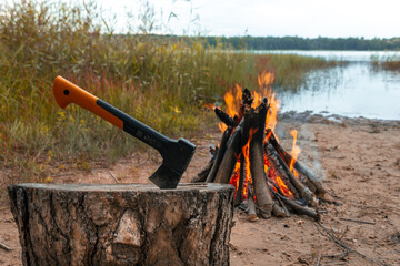 The axe is stuck in a log. Chopping wood for a fire on the background of the lake. Survival in the forest during a hike. Making a fire.  A sharp axe. A woodcutter's tool. A modern axe.