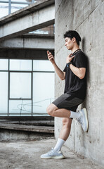 Young Asian Sportsman leaning against the wall is using mobile phone